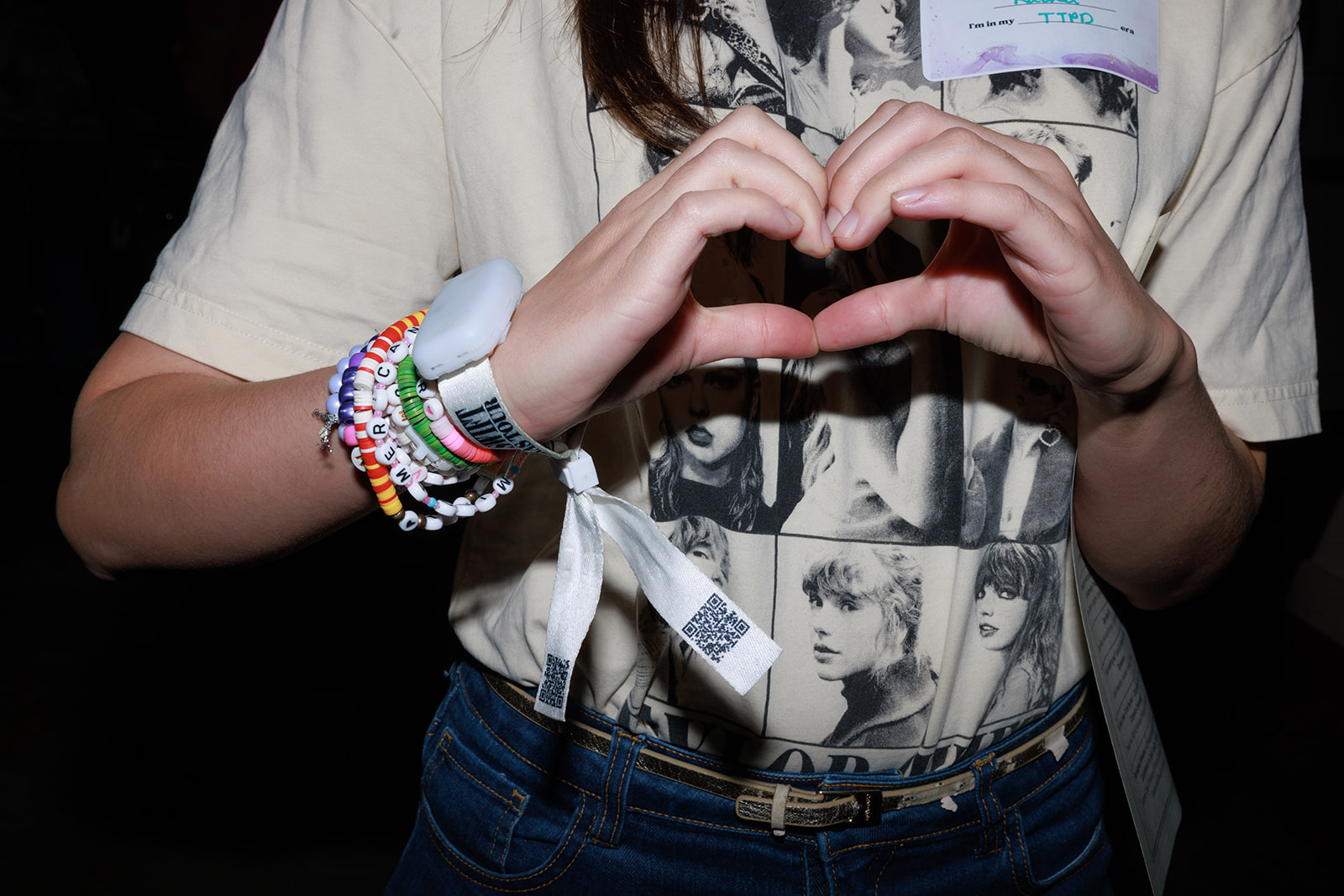 A student makes a heart with her hands and shows off her friendship bracelet.