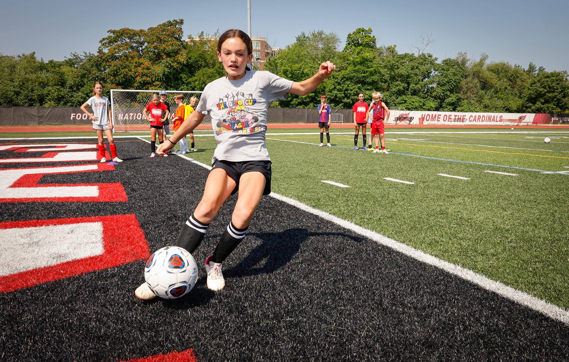 A young woman kicks a soccer ball during North Central College's summer soccer camp.