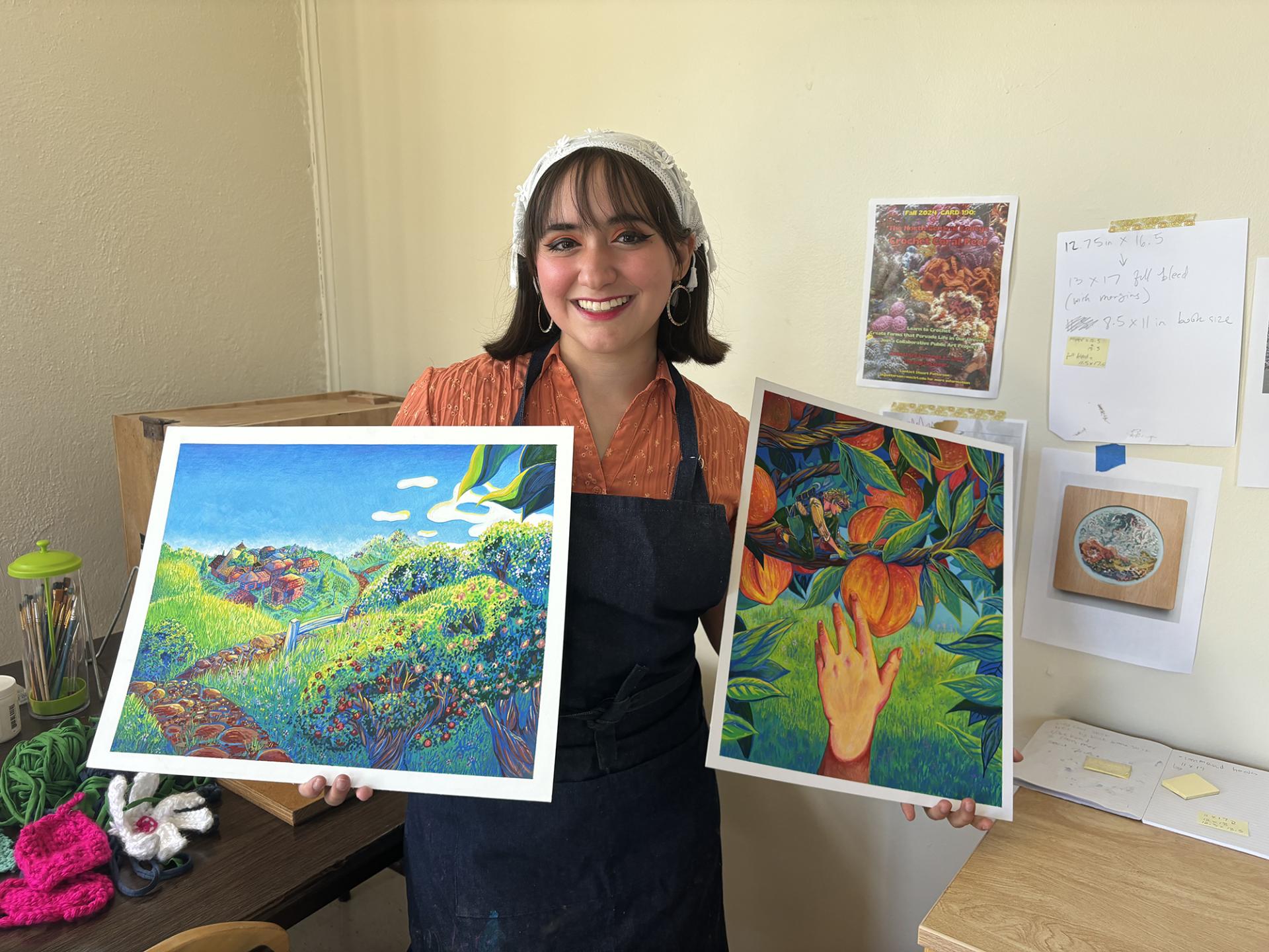 Andrea Peguero Gonzalez displaying two of her paintings.