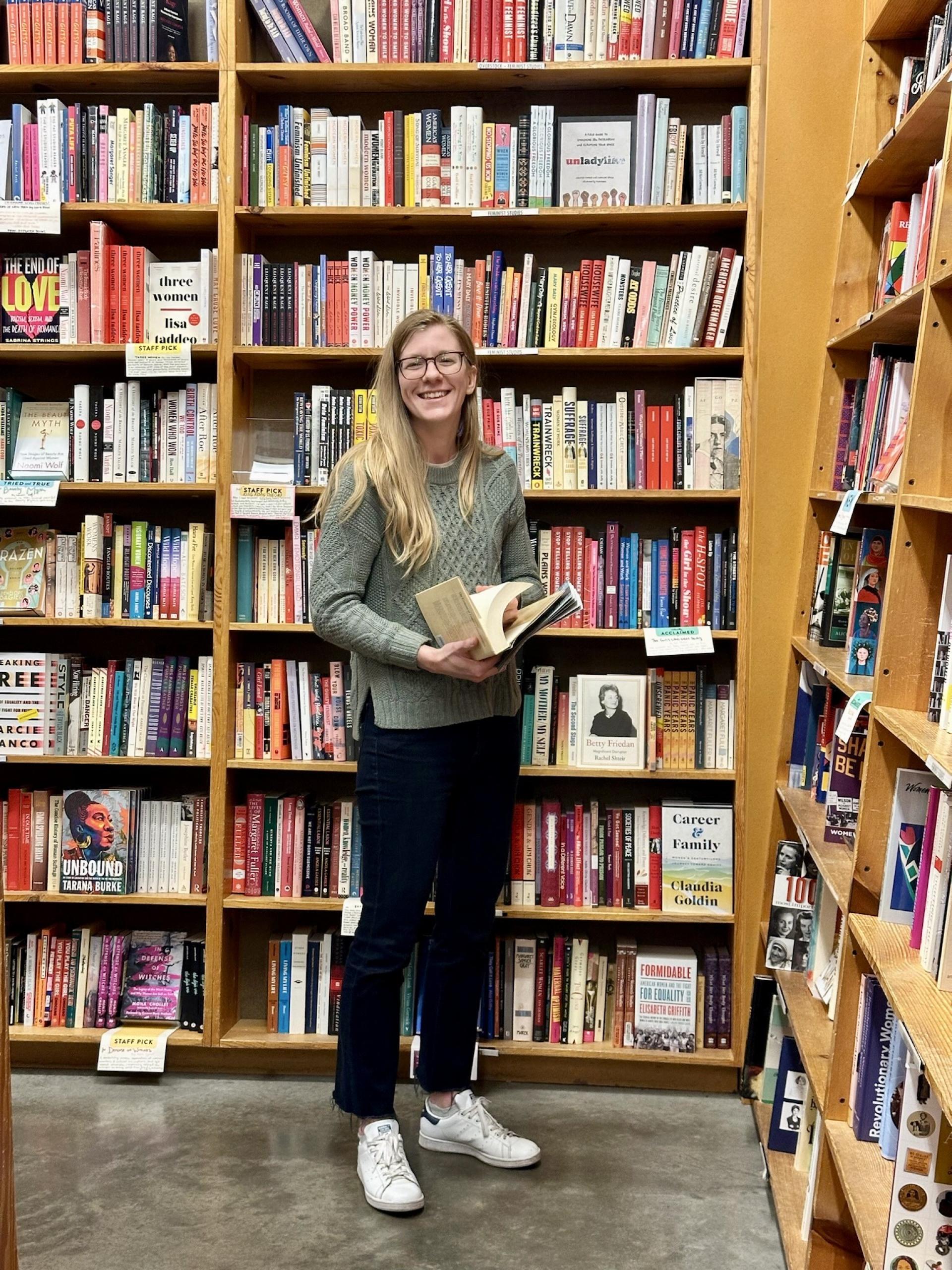 Elizabeth Kulisek ’17 is standing in a bookstore holding a book open.