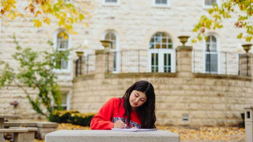 A North Central College student sitting outside writing in a notebook.